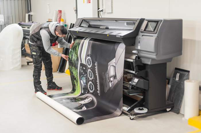 Technician worker operator works on large premium industrial printer and plotter machine in digital printshop office