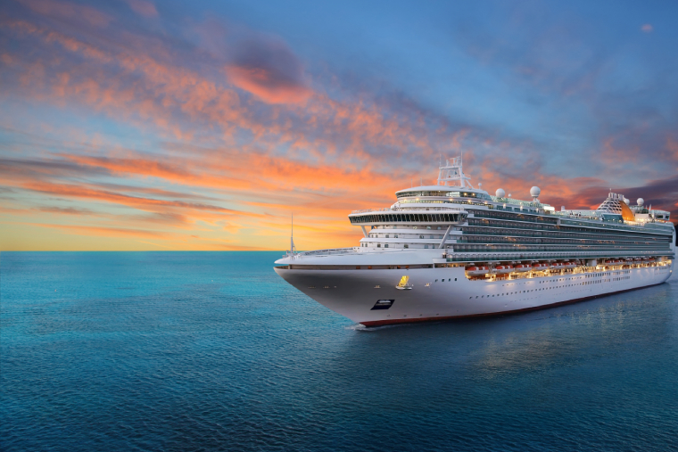 Large white cruise ship sailing on calm blue ocean during a vibrant sunset with colorful clouds in the sky.